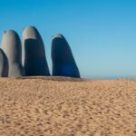 The Hand of Punta del Este sculpture emerges from the sand under a clear blue sky.